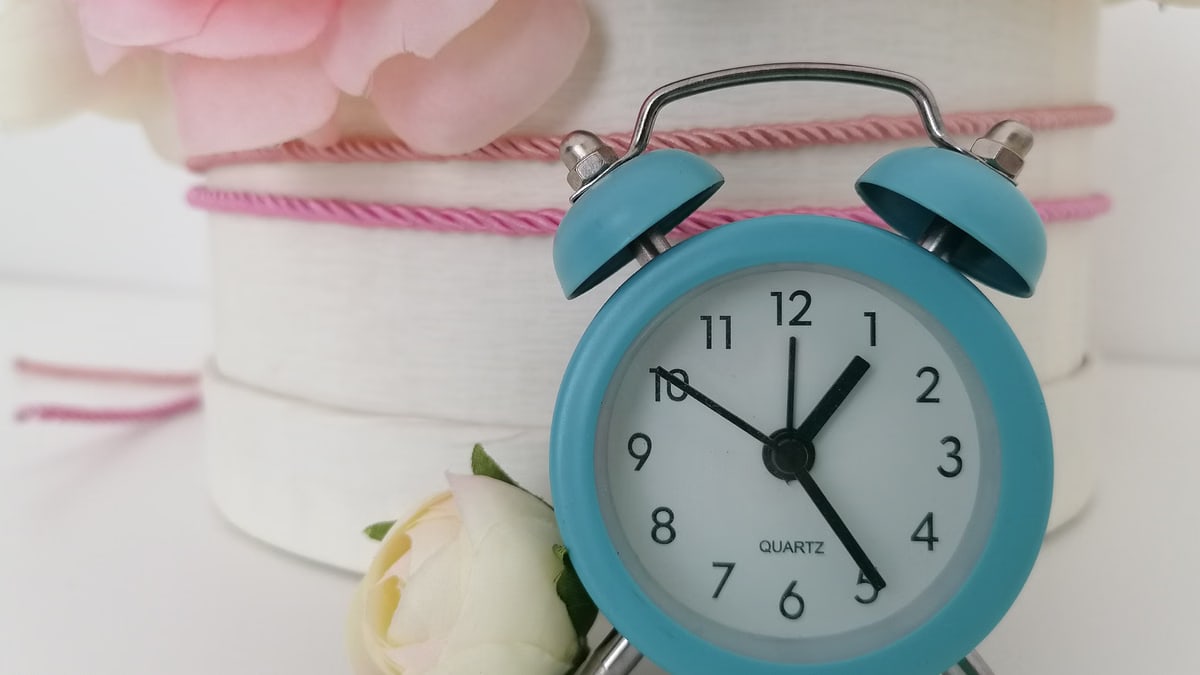 Charming blue analog alarm clock against a background of delicate flowers.
