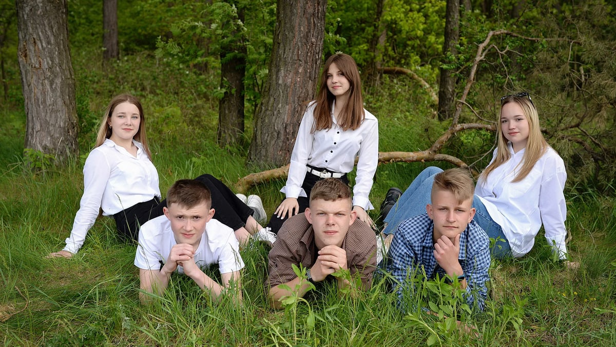 A group of young adults posing together on grass in a forest setting.